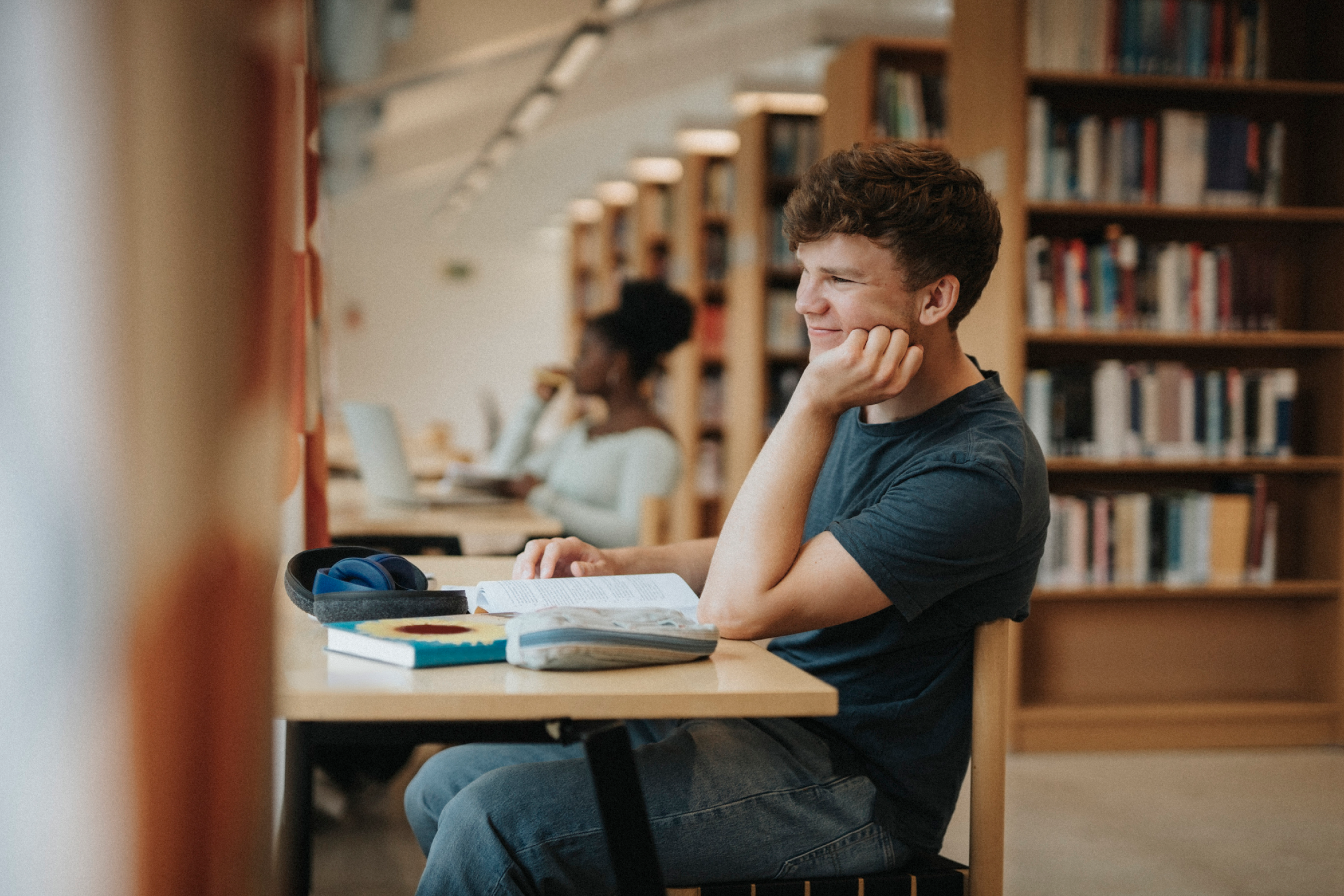Um estudante estudando em uma mesa com livros e um laptop em uma biblioteca.